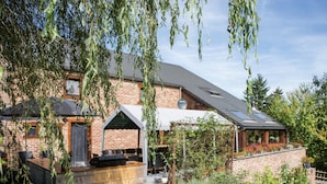 A brick house with a covered patio, a garden, and a solar panel on the roof. - Atmospheric Holiday Home in Durbuy With Sauna (Durbuy)