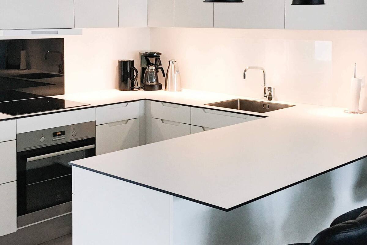 Une cuisine moderne avec des meubles blancs, un plan de travail noir, un four encastré, une machine à café et un évier.