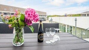 A table with a bottle of wine, glasses, and a vase with flowers on a rooftop terrace. - 8 Person Holiday Home in Ringkobing (Ringkobing)