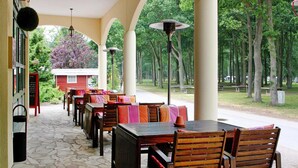 Un patio esterno con pavimento in pietra, tavoli e sedie di legno, e un edificio rosso sullo sfondo.