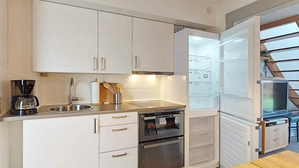 A modern kitchen with white cabinets, stainless steel appliances, and a wooden dining table.