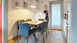 A modern dining area with a wooden table and black chairs, a ceiling light, and framed artwork on the walls.