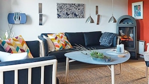A modern living room with a black sofa, colorful pillows, a round coffee table, and a fireplace.