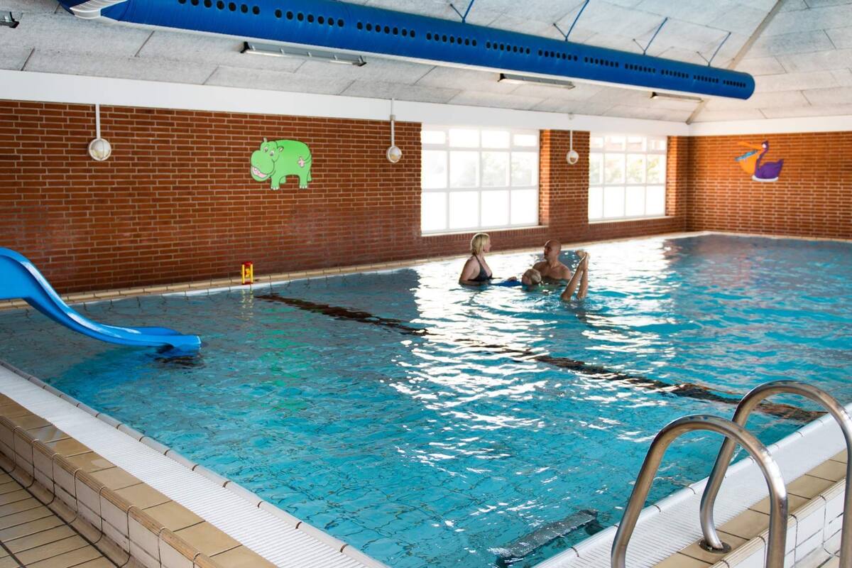Une piscine intérieure avec un toboggan bleu, un mur en briques et un plafond équipé de conduits de ventilation.