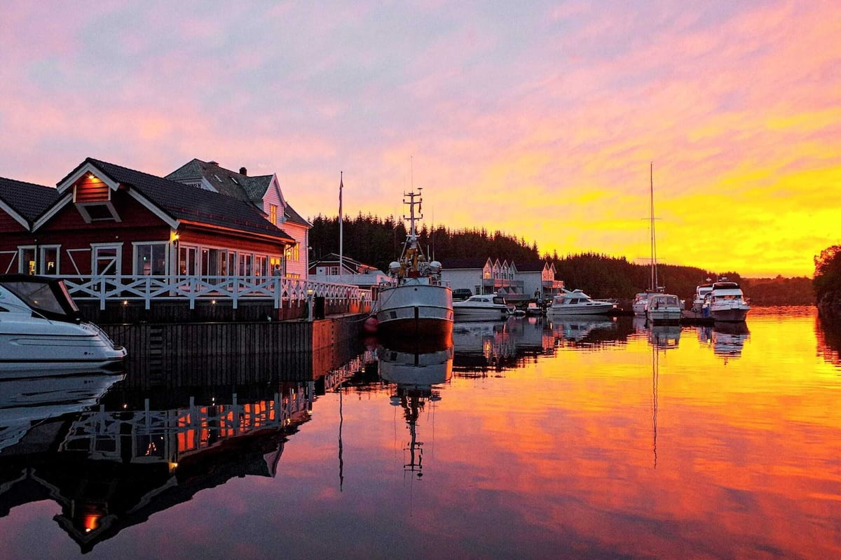 A waterfront property with a docked boat, a house with a porch, and a forested background.