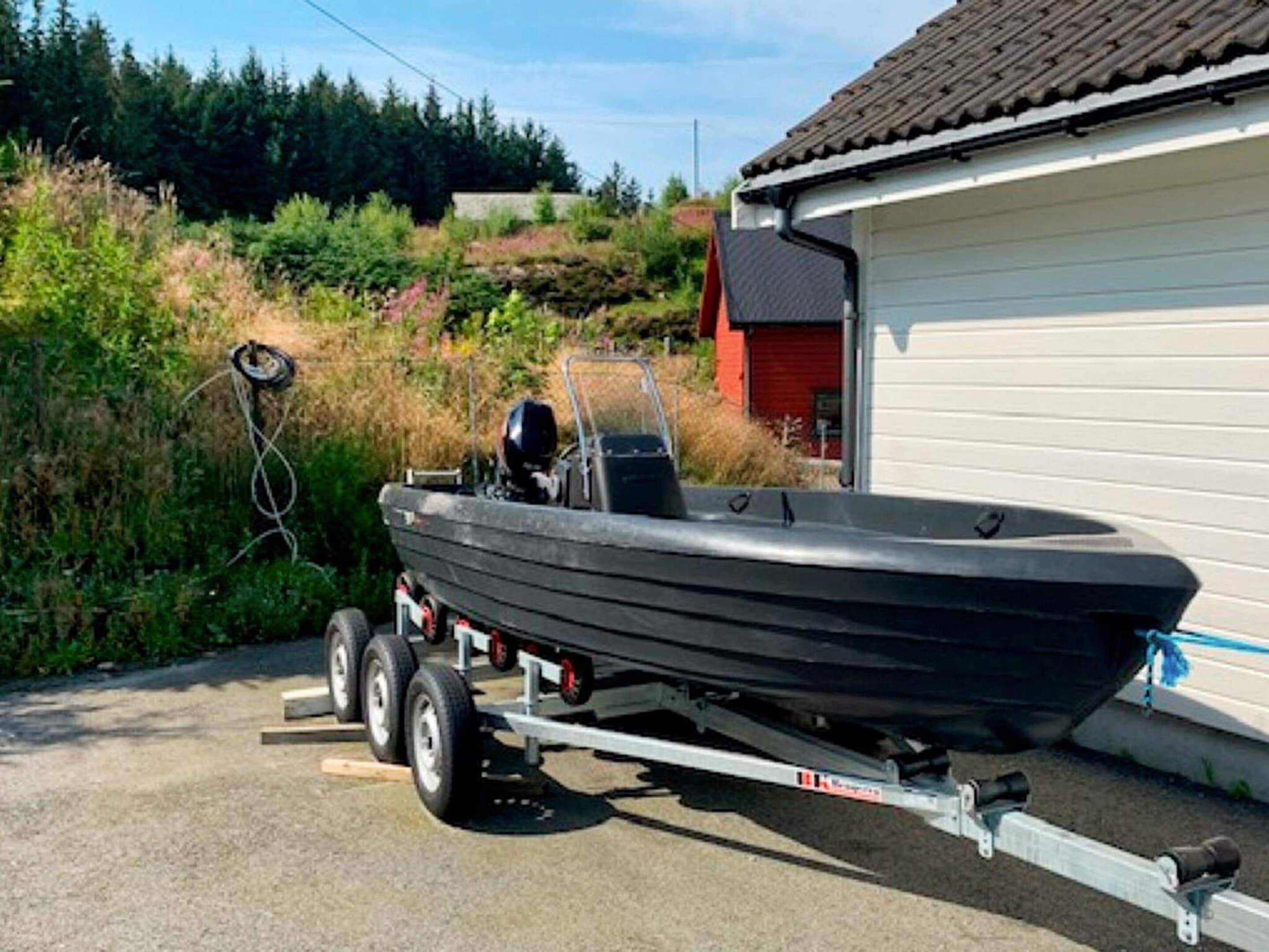 Un barco a motor negro sobre un remolque estacionado frente a una casa con puerta roja.