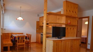 A compact kitchen with wooden cabinets, a dining area with a table and chairs, and a TV on a wooden counter. - Amazing Apartment in Cavalese With Shared Terrace (Cavalese)