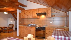 A kitchen with wooden cabinets, a dishwasher, and a stove. There is a dining area with a table and chairs. - Amazing Apartment in Cavalese With Shared Terrace (Cavalese)
