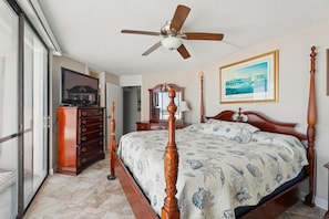A bedroom with a four-poster bed, a ceiling fan, a television, and a framed picture on the wall.