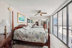 Un dormitorio con una cama grande, un ventilador de techo, un aparador y vistas a través de una puerta corrediza de vidrio.