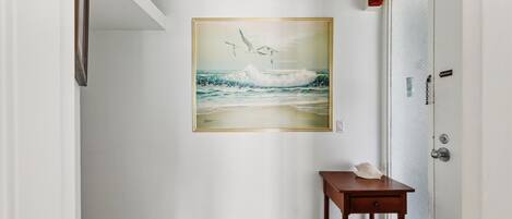A hallway with a painting of seagulls and waves on the wall, a small wooden table, and a door with a security device.