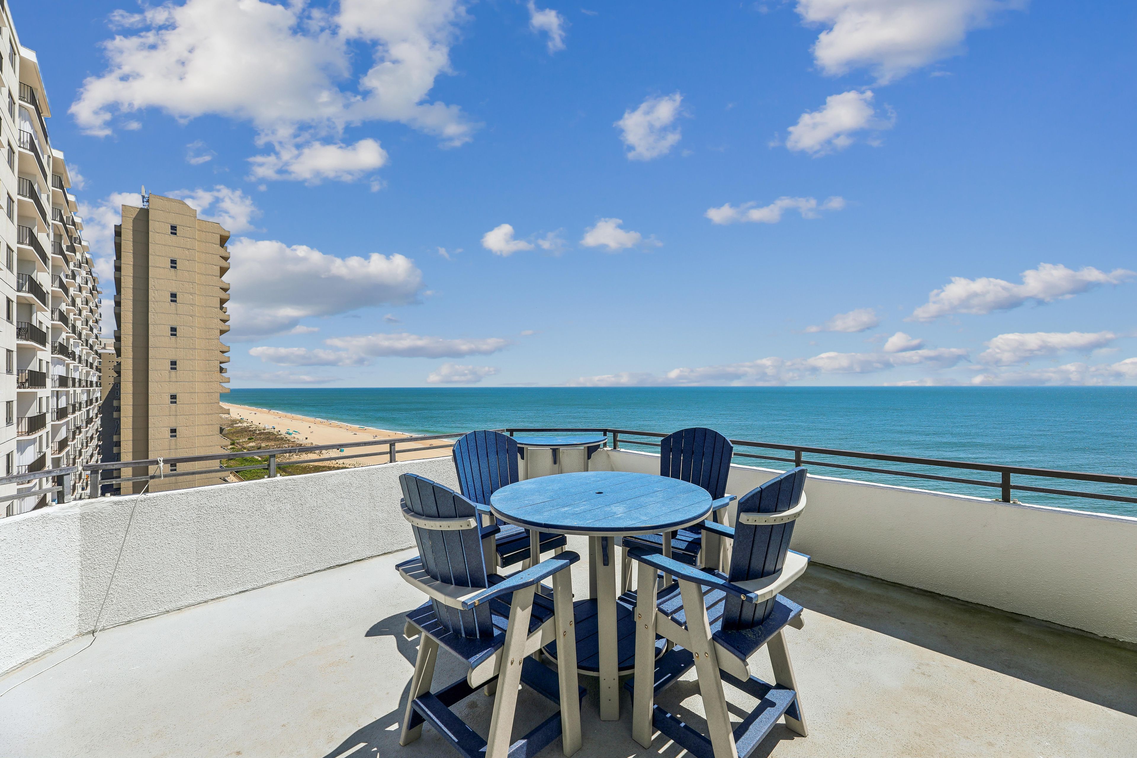 Un balcon avec une table ronde et des chaises, donnant sur une plage et l’océan.