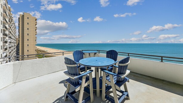 Un balcon avec une table ronde et des chaises, donnant sur une plage et l’océan.