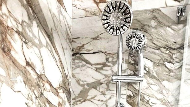 Une salle de bain avec une douche, un miroir et un mur en marbre.