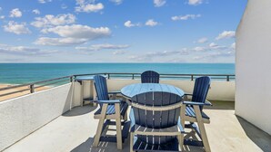 Un balcon avec une table et des chaises donnant sur une plage et l’océan.