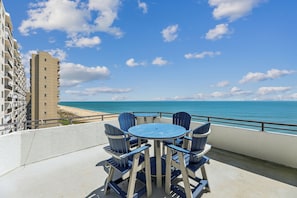 Ein Balkon mit rundem Tisch und Stühlen, der Blick auf einen Strand und das Meer freigibt.