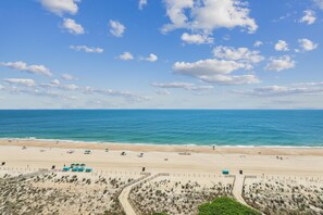 A beach with a clear sky, calm sea, and a fenced area with beach chairs and umbrellas. - Includes Xplorie Activities and Linens. PYRAMID - 1BR oceanfront condo w/outdoor pool. (Ocean City)