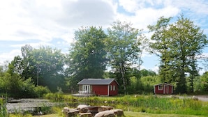 A red cabin with a porch, surrounded by a natural landscape with trees and a small pond. - 4 Person Holiday Home in Smedstorp (Smedstorp)