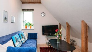 A cozy living room with a blue sofa, a small table with a vase of flowers, a television, and a window with plants. - 6 Person Holiday Home in Ribe (Ribe)