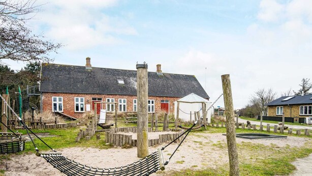 A sandy area with a hammock and wooden structures, a brick building with a red door, and a clear sky. - 6 Person Holiday Home in Ribe (Ribe)