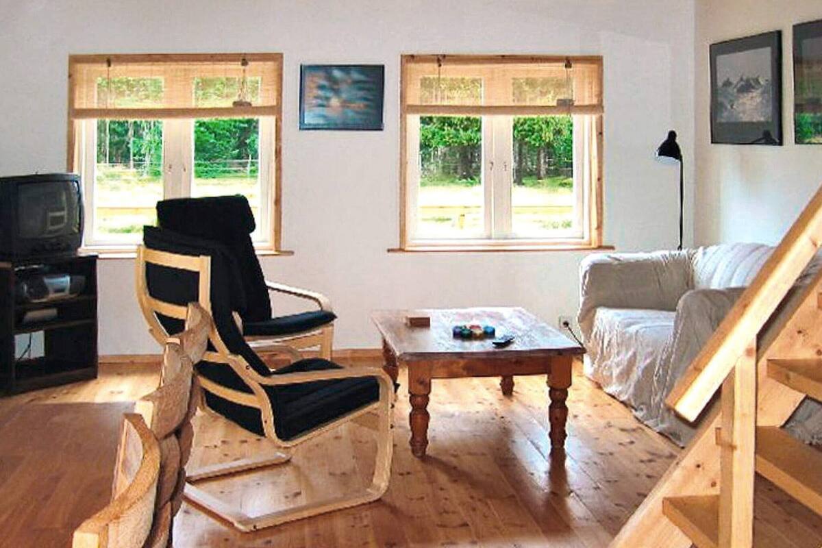 A wooden-floored living room with a black and white striped chair, a white sofa, a small wooden coffee table, and a TV stand.