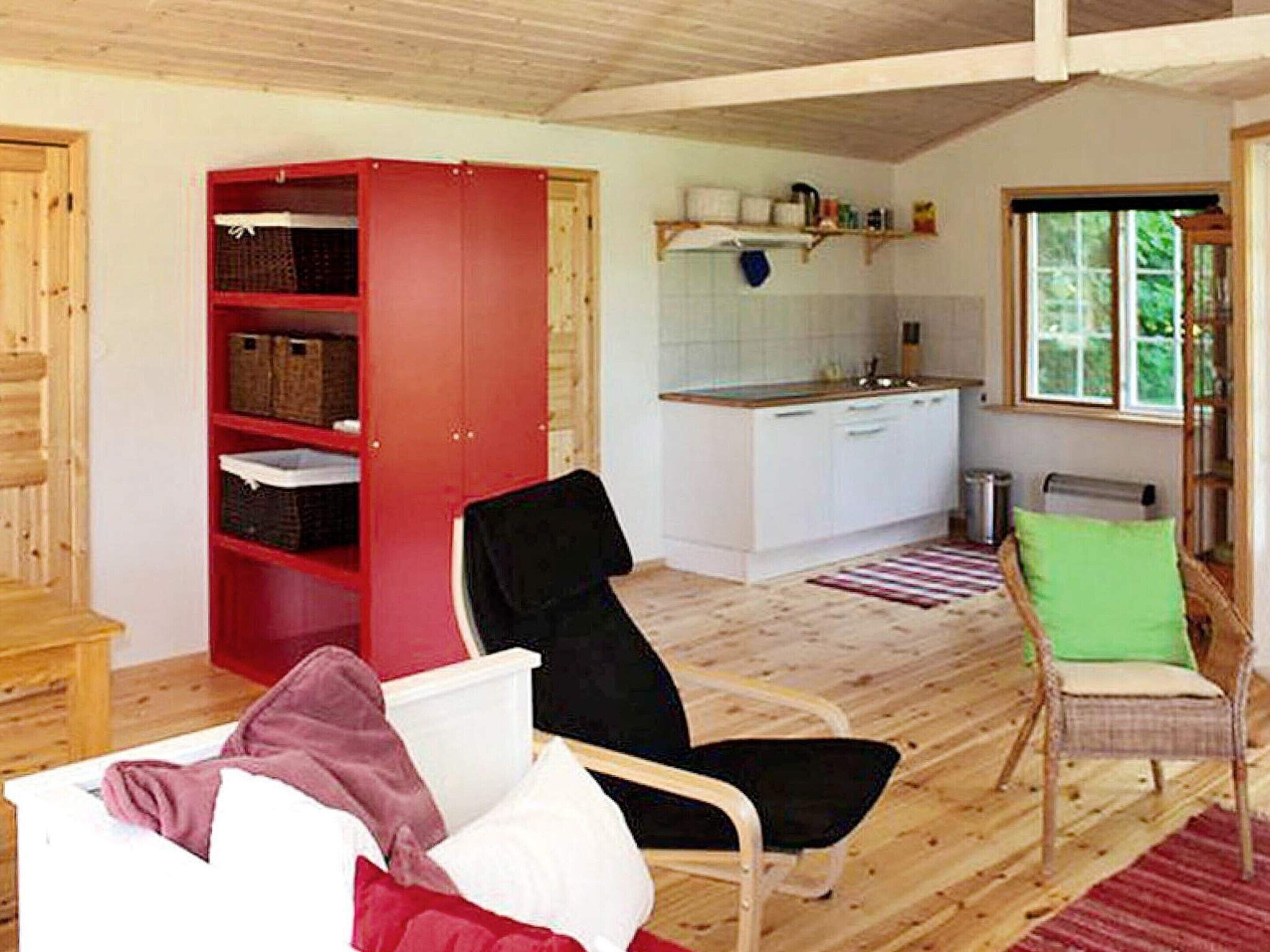 Una habitación con un armario rojo, una silla negra, una silla verde, un sofá blanco y una zona de cocina con ventana.
