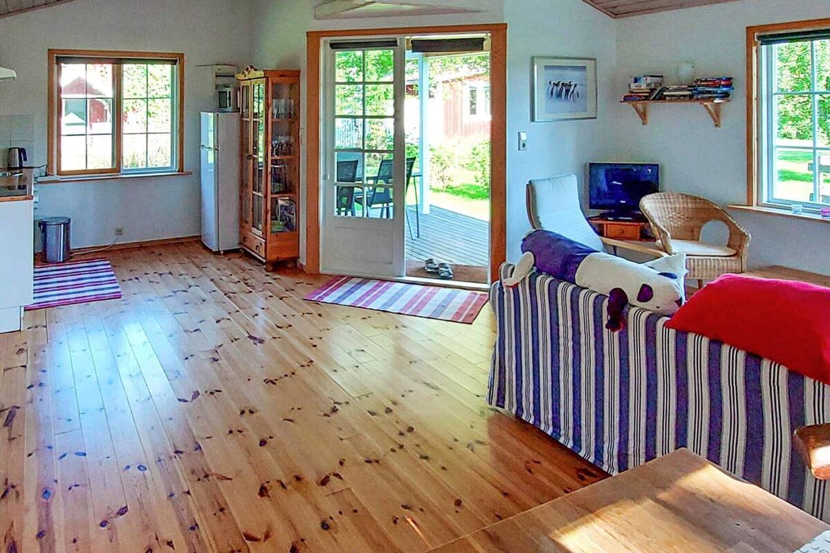 A spacious living area with a wooden floor, a striped sofa, a television, and a bookshelf.