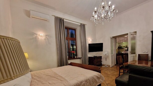 A hotel room with a bed, a TV, a fan, a chandelier, and a dining area. - Apartment in the city center (Kraków)