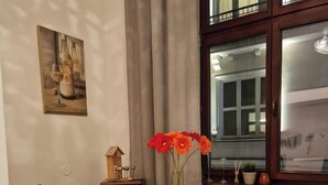 A dining area with a round wooden table, two chairs, a vase with flowers, a small wooden house decoration, and a window with curtains. - Apartment in the city center (Kraków)