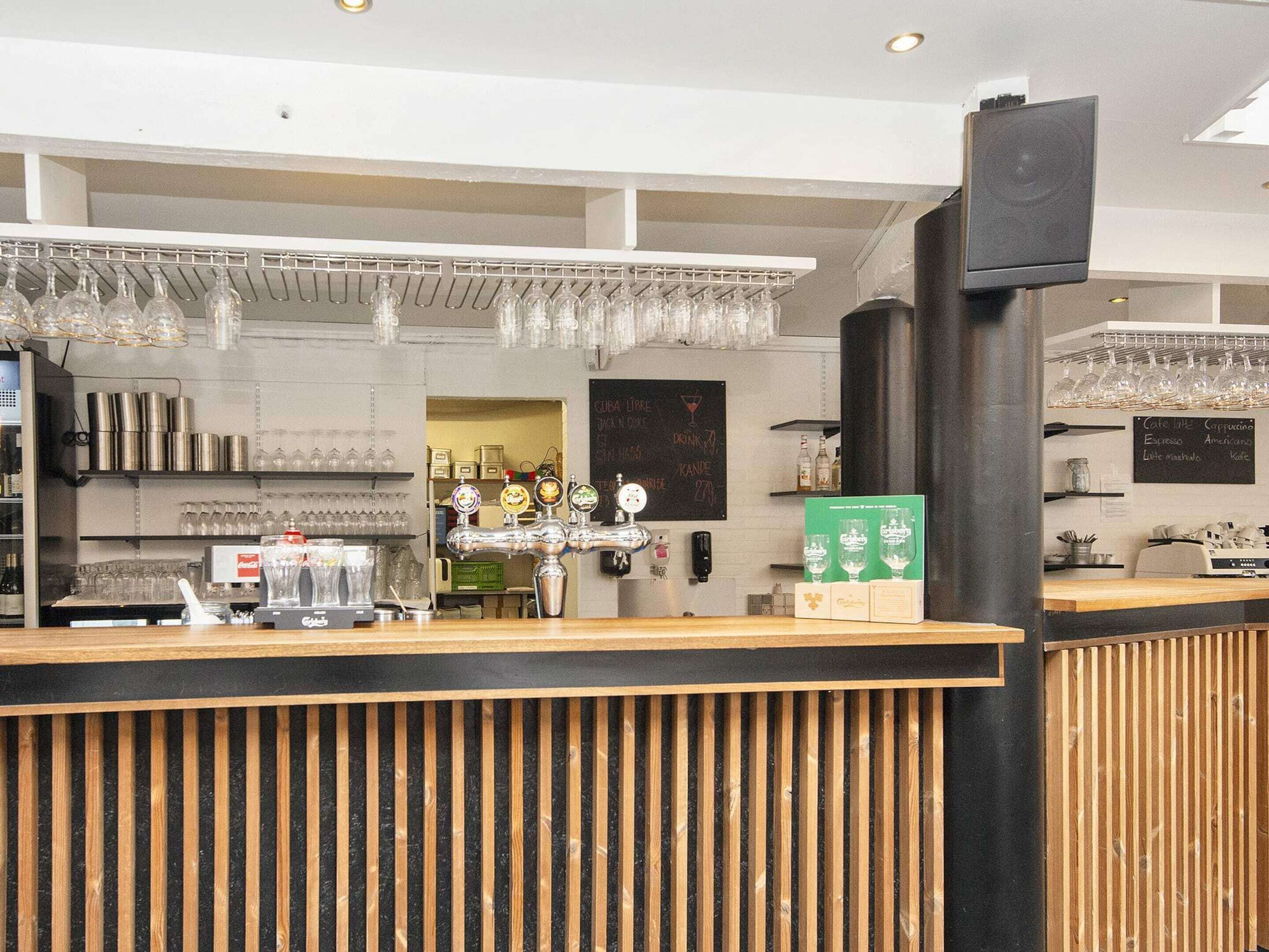 Uma área de bar com balcão de madeira, várias torneiras e um cardápio em lousa.