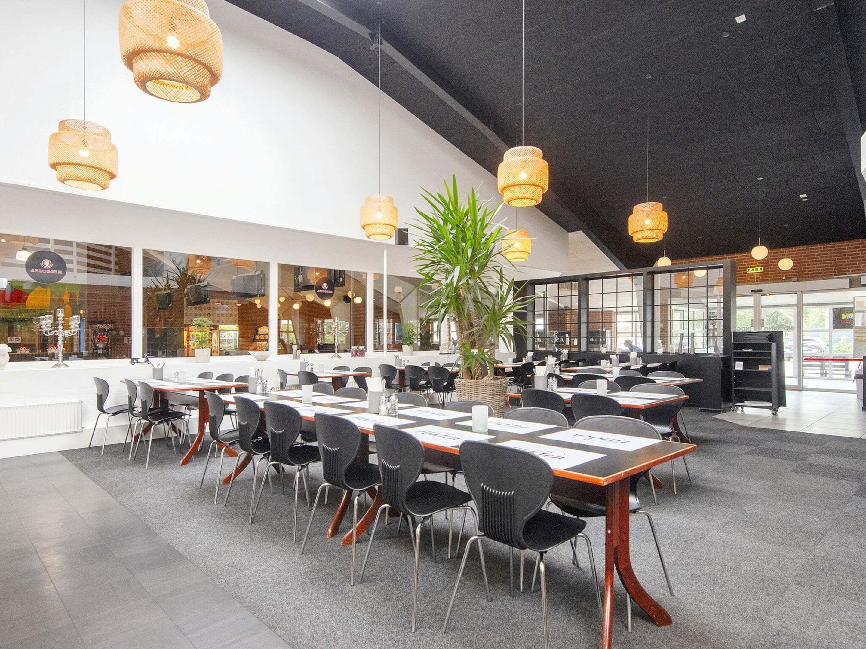 A spacious dining area with multiple tables and chairs, large windows, and hanging wicker pendant lights.