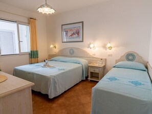 Una habitación con dos camas, una mesita de noche con lámpara, un cuadro enmarcado en la pared y una ventana con cortinas.
