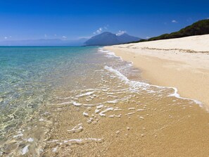 Una spiaggia con acque cristalline e poco profonde, una riva sabbiosa e una montagna sullo sfondo.