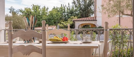 A wooden table with a plate of fruit and a cup, set against a backdrop of trees and a building with a tiled roof.
