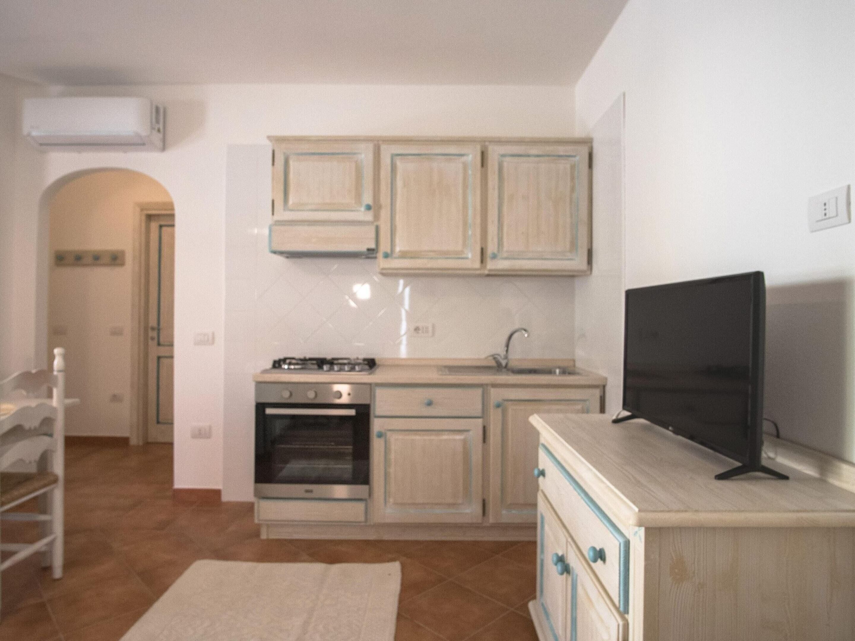 A compact kitchen with a stove, oven, sink, and a flat-screen TV on a wooden cabinet.