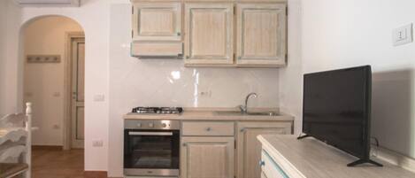 A compact kitchen with a stove, oven, sink, and a flat-screen TV on a wooden cabinet.