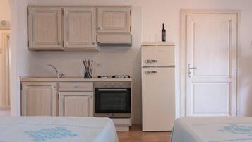 A compact kitchen with wooden cabinets, a stove, oven, and a refrigerator. There are two beds with matching covers.