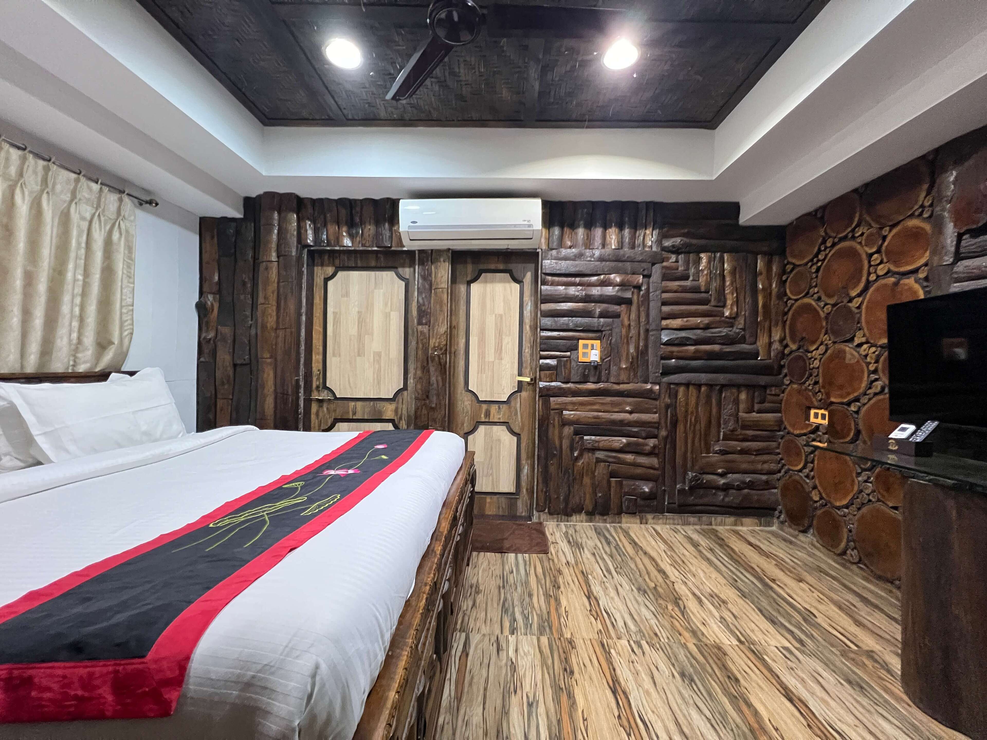 Een slaapkamer met een bed, houten wandbekleding, een airconditioning en een televisie op een glazen tafel.