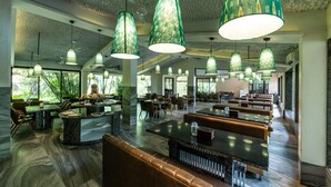 Tilava ravintola, jossa on korkeat katot, suuret ikkunat ja vihreäkuvioidut riippuvalaisimet.