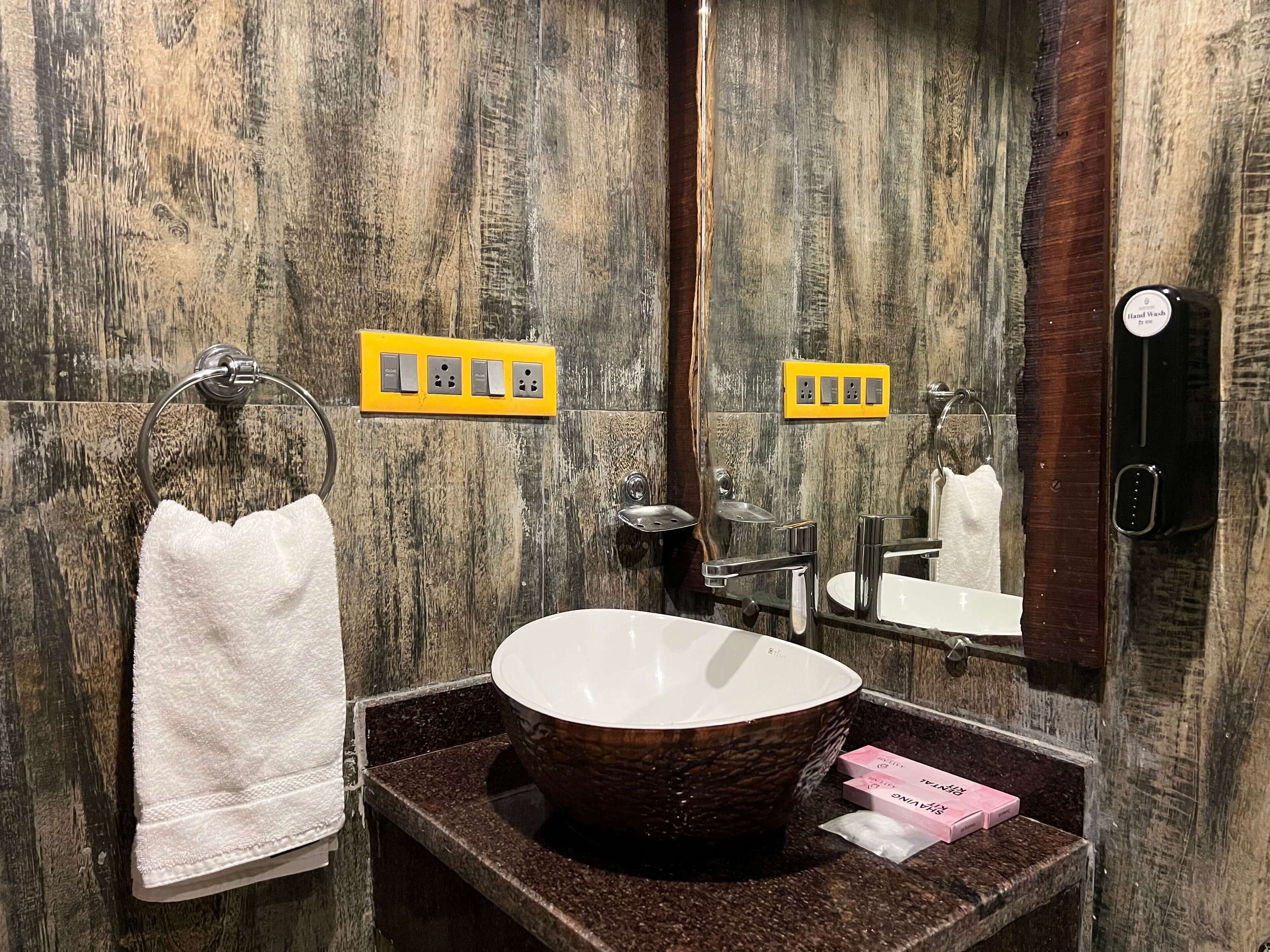 A bathroom with a wooden wall, a white sink, a mirror, and a towel rack.