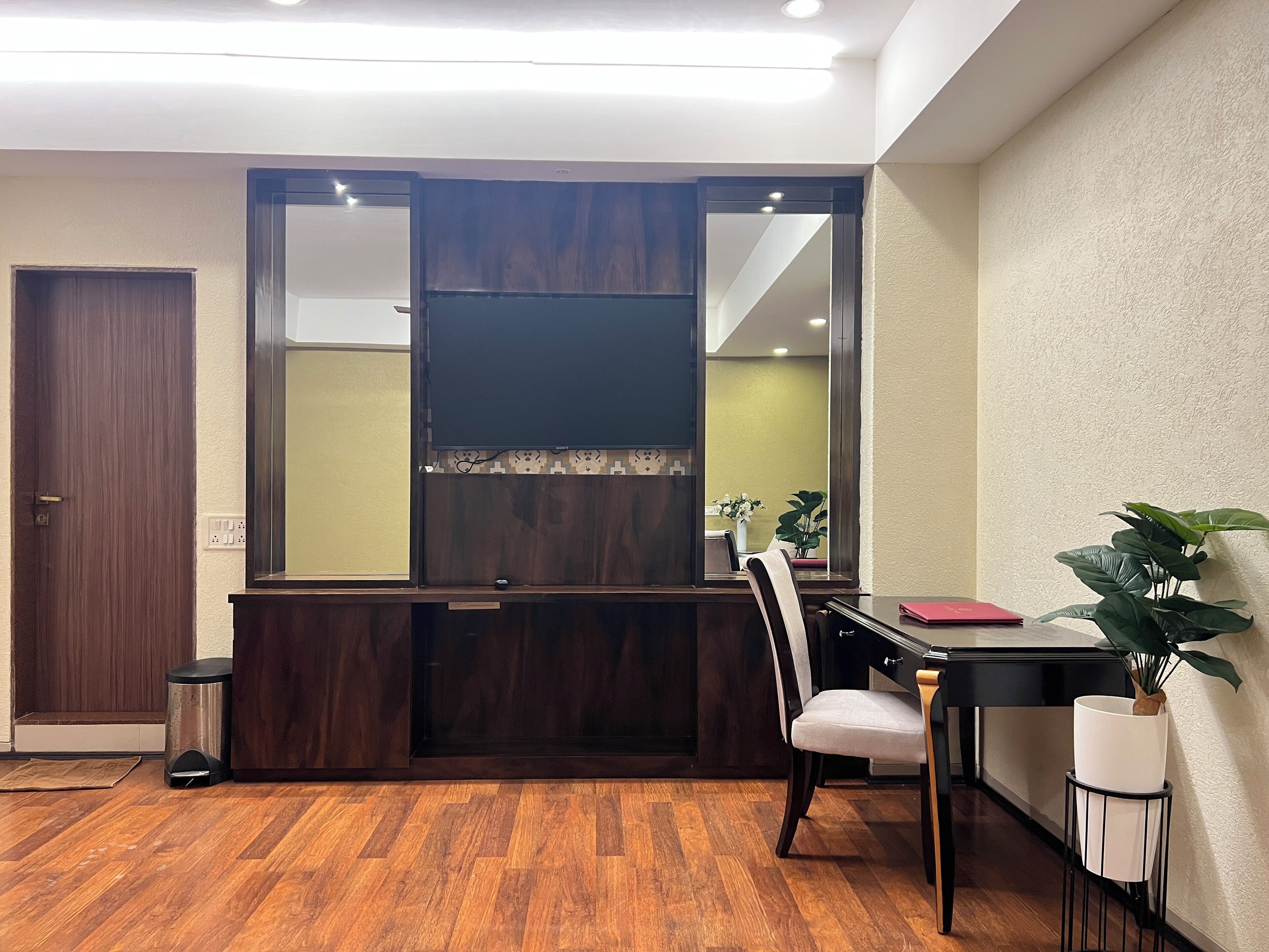 A room with a wooden desk, a chair, a potted plant, and a mirror.