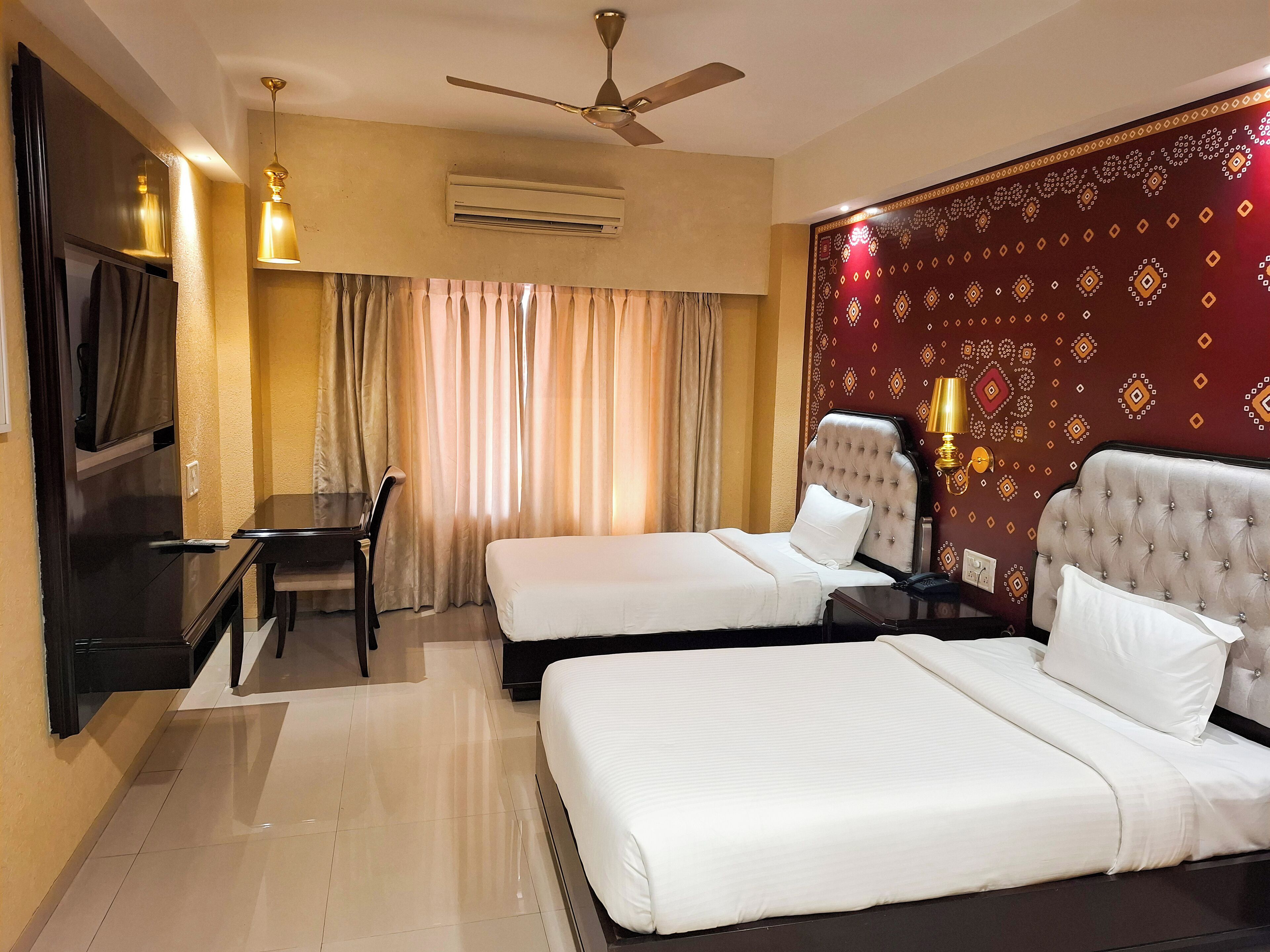 A hotel room with two beds, a desk, a chair, an air conditioning unit, and a ceiling fan.