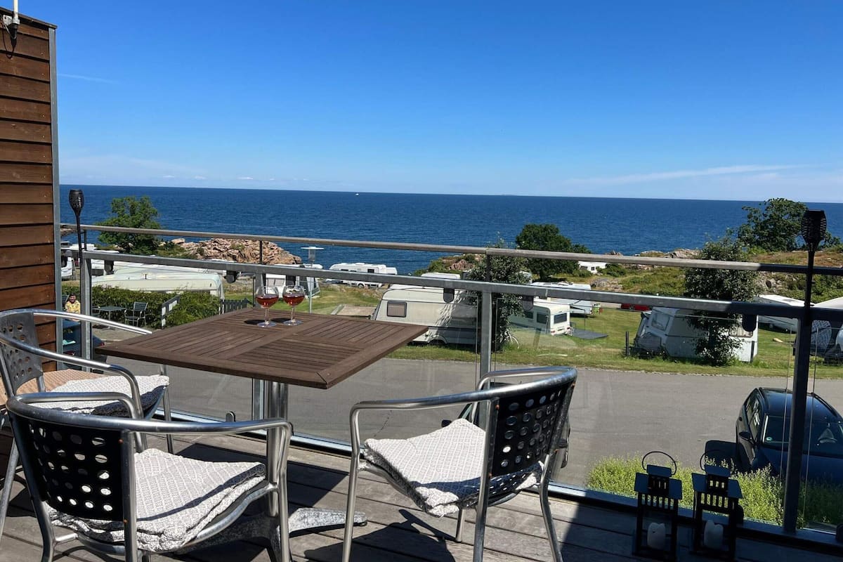 Ein Balkon mit Tisch und Stühlen, der auf eine Küstenlandschaft mit Wohnmobilen und blauem Himmel blickt.