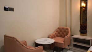 A room with two pink upholstered chairs, a round marble table, a small white nightstand, and a wall-mounted light fixture. - Bageecha Resort Pushkar (Pushkar)
