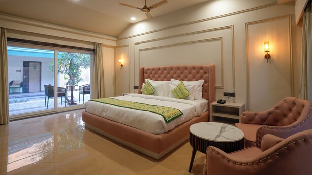 A spacious bedroom with a large bed, a sitting area with a chair and a small table, and a balcony with outdoor furniture. - Bageecha Resort Pushkar (Pushkar)
