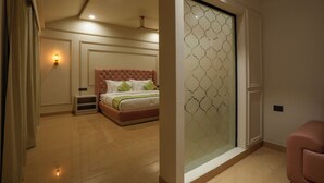 A bedroom with a bed, a nightstand, a wall-mounted light, a ceiling fan, and a sliding glass door with a geometric pattern. - Bageecha Resort Pushkar (Pushkar)