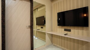 A bathroom with a mirror, a television mounted on the wall, and a shelf with a remote control. - Bageecha Resort Pushkar (Pushkar)