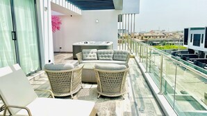 A balcony with wicker furniture, a hot tub, and a glass railing overlooking a cityscape. - Lekki Villas (Lekki)