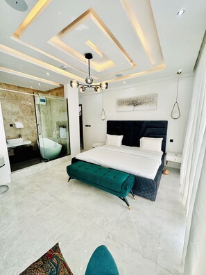 A modern bedroom with a large bed, a bench, a shower area, and a ceiling light fixture. - Lekki Villas (Lekki)