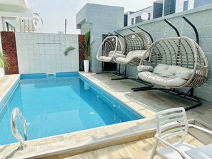 A swimming pool with two wicker chairs and a white plastic chair. - Lekki Villas (Lekki)